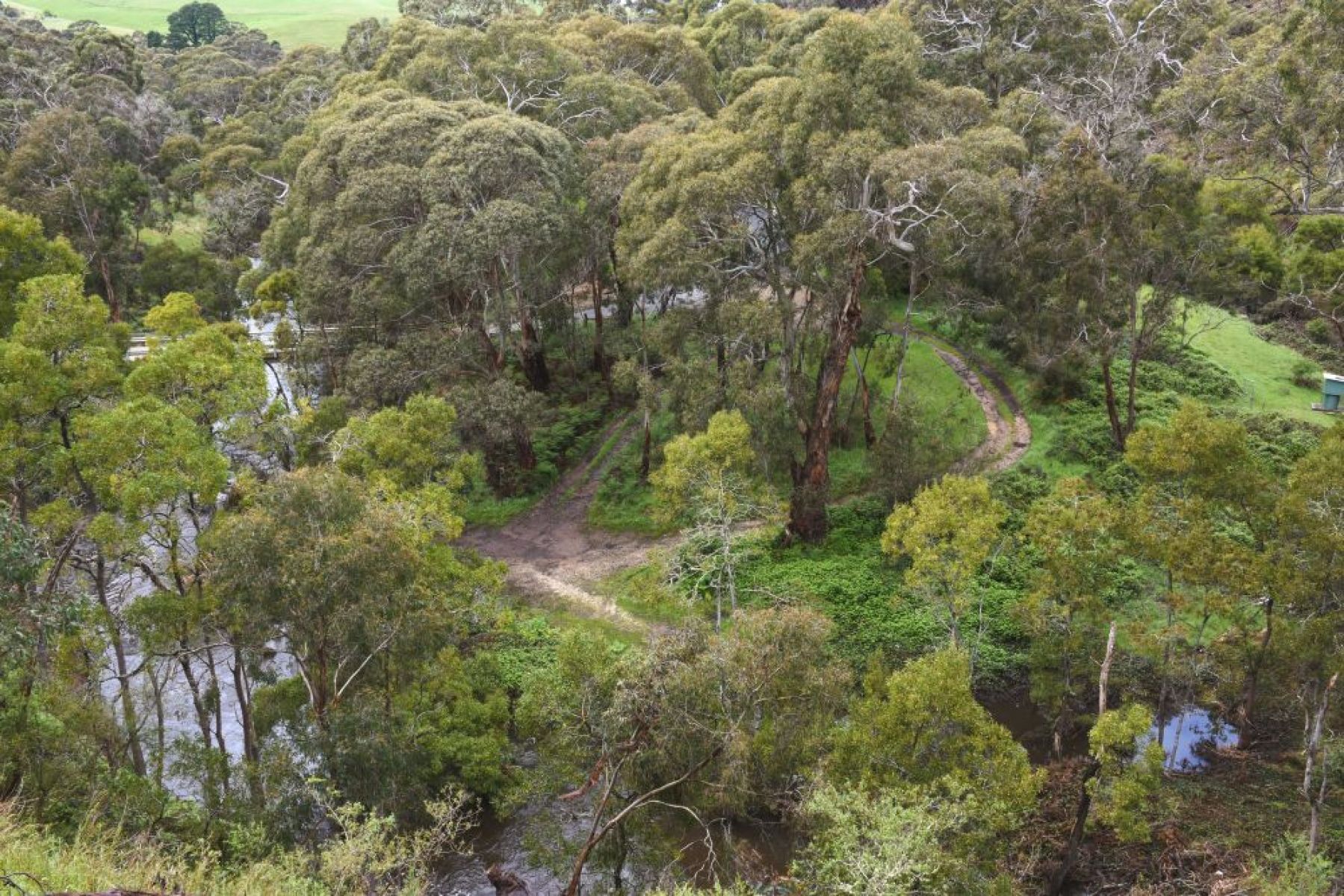 An aerial view over an opening in bushland with a river running through.