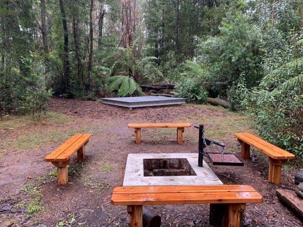 A fit pit in the camping area. surrounded by 4 wooden benches. 