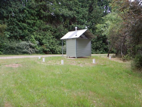 A metal toilet block with lush green shrubbery in the background.