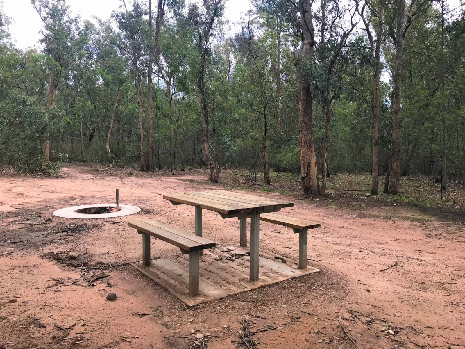 A brown dusty campground area with a picnic table and fire pit