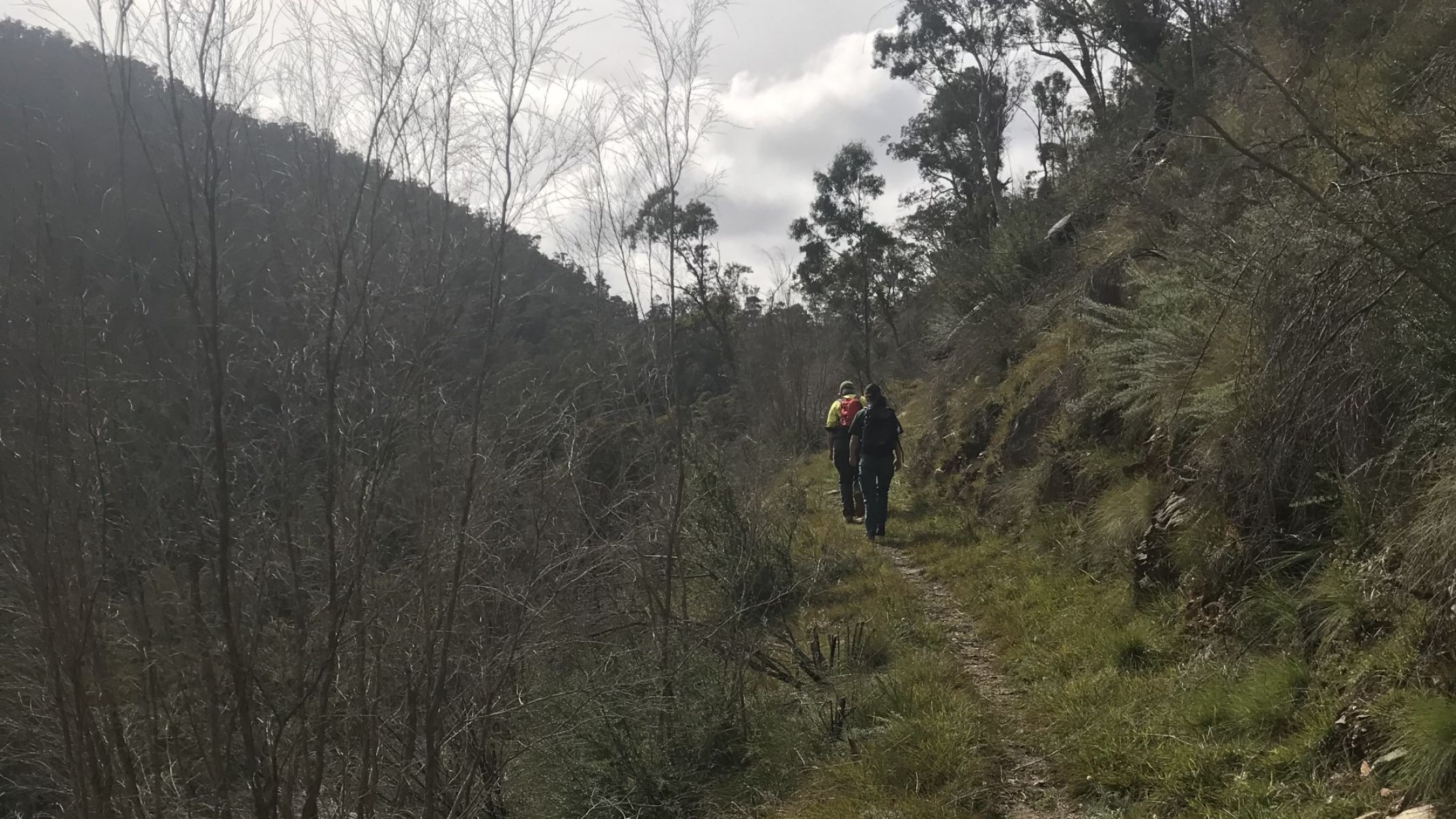 Two people walk along a dirt track on the side of a hill