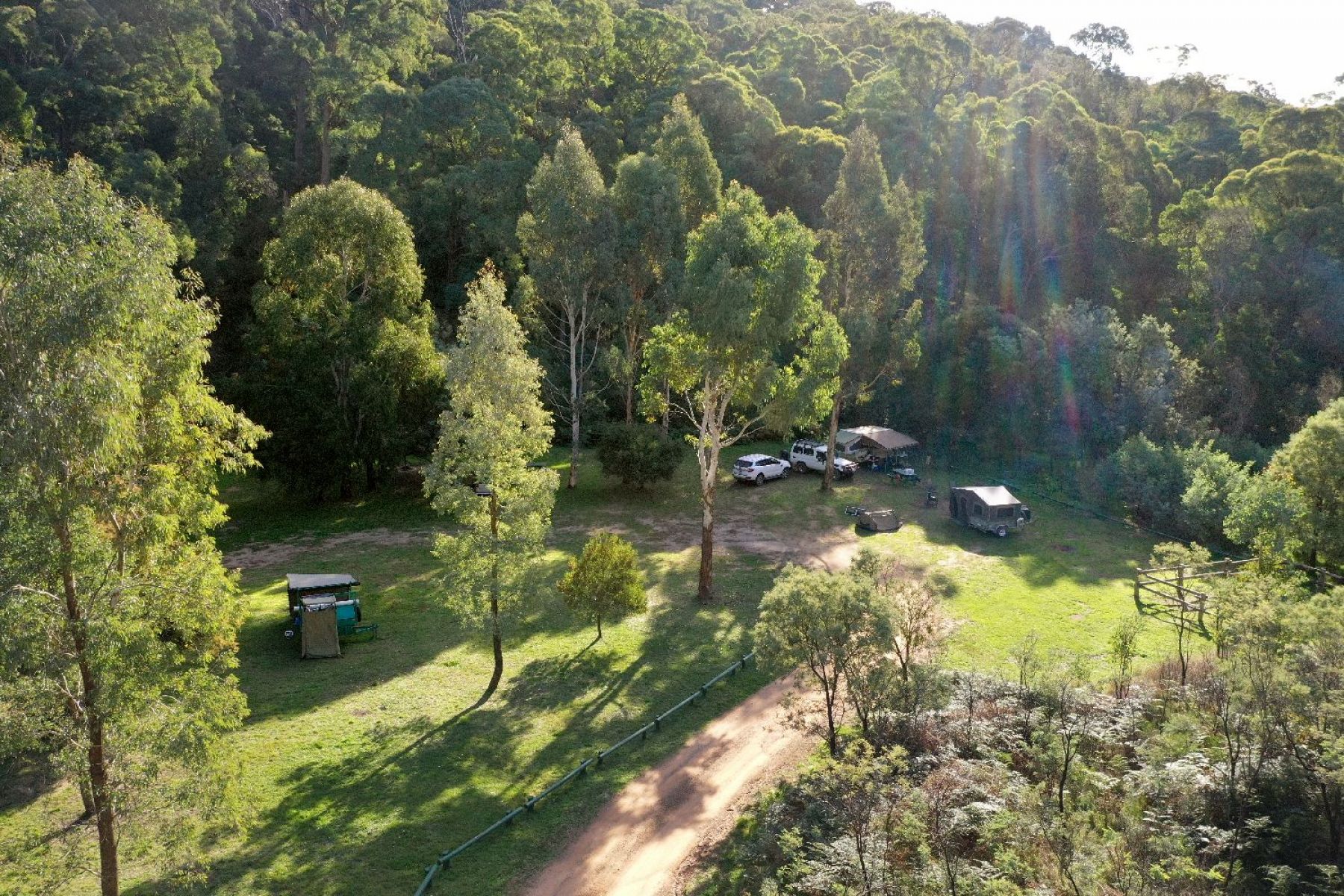 An aerial view of a group of campers set up under the trees in a grassy spacious area