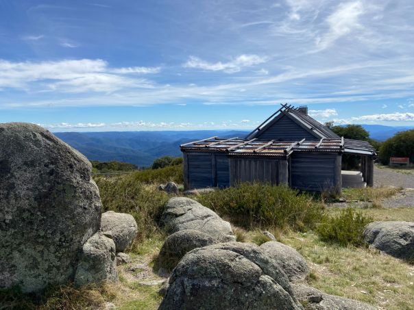 An old timber hut sits on the top of a mountain with sprawling views