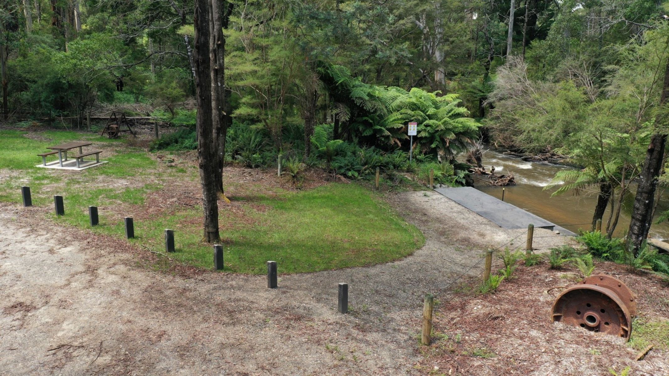 A picnic table and historic timber mill relics sit alongside a river