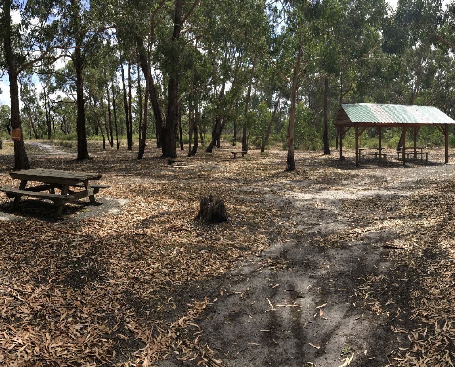 A dirt covered area with picnic tables and a picnic shelter