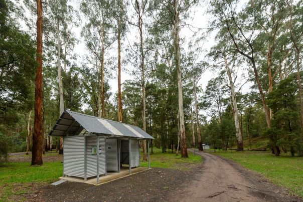 An amenity block at Running Creek. A grey building surrounded by trees. A track is out the front of the structure. 