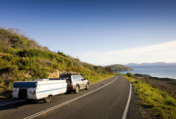 A caravan is towed by a 4WD vehicle along a coastal road