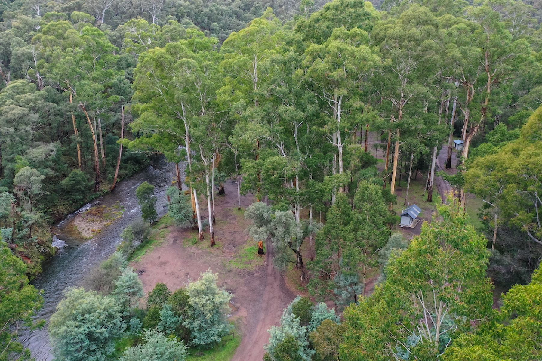 An aerial view over a campground. A dirt road runs thorugh the middle and two metal toilets blocks can be seen either side.