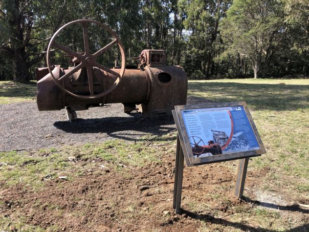 A large, rusted vintage boiler with a wooden interpretive sign in front.