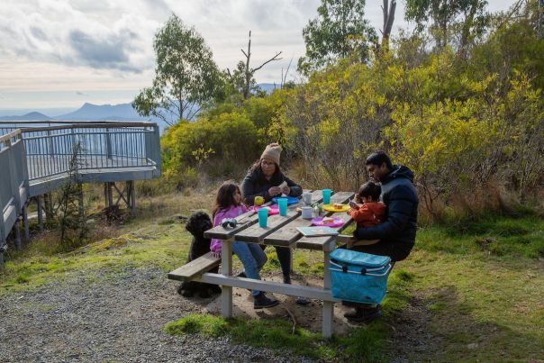 A family enjoy a picnic at the top of a mountain with a lookout behind them