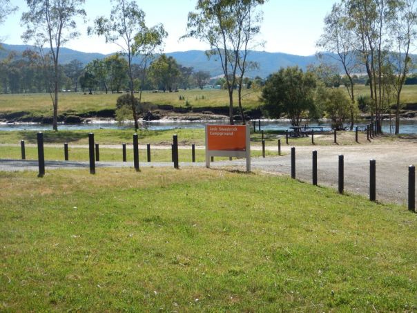 Grassy campground with wooden bollards overlooking a flowing river and tree covered mountains in the background.