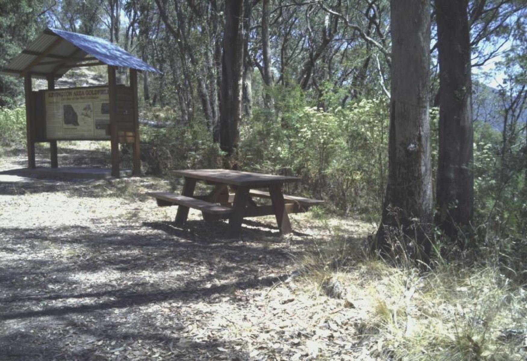 A wooden picnic table near an information signage in a shady bush area