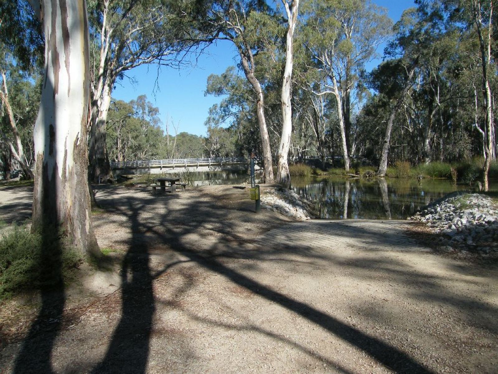 A ramp leading to the river, where you can enter for water activities. A bridge in the background. Gum trees surrounding the lake.