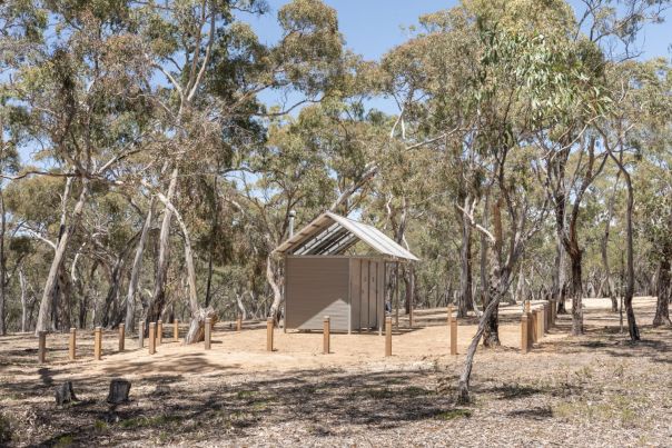 A small metal toilet block surrounded by bollards and trees