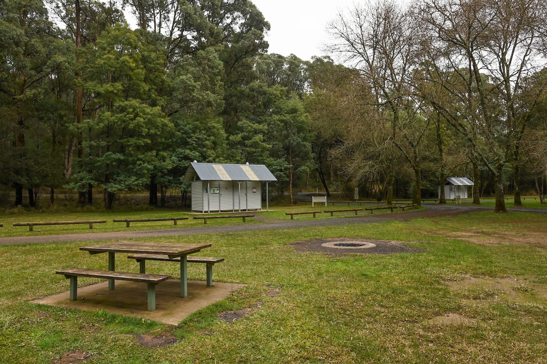 A grassy and flat campground with two mteal toilet blocks and a wodden picnic table in the foreground.