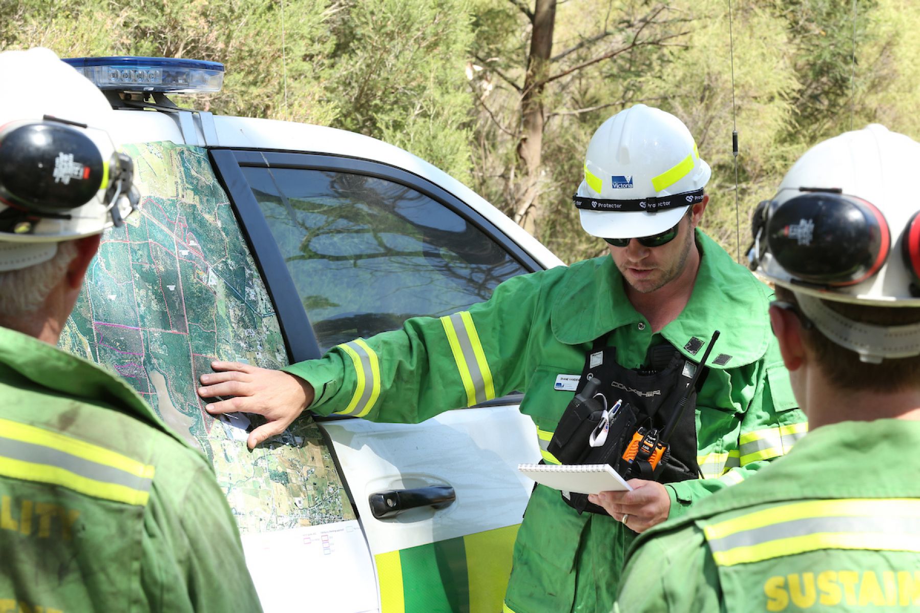 A team of forest firefighters look at a map beside a vehicle as part of planned burns preapration