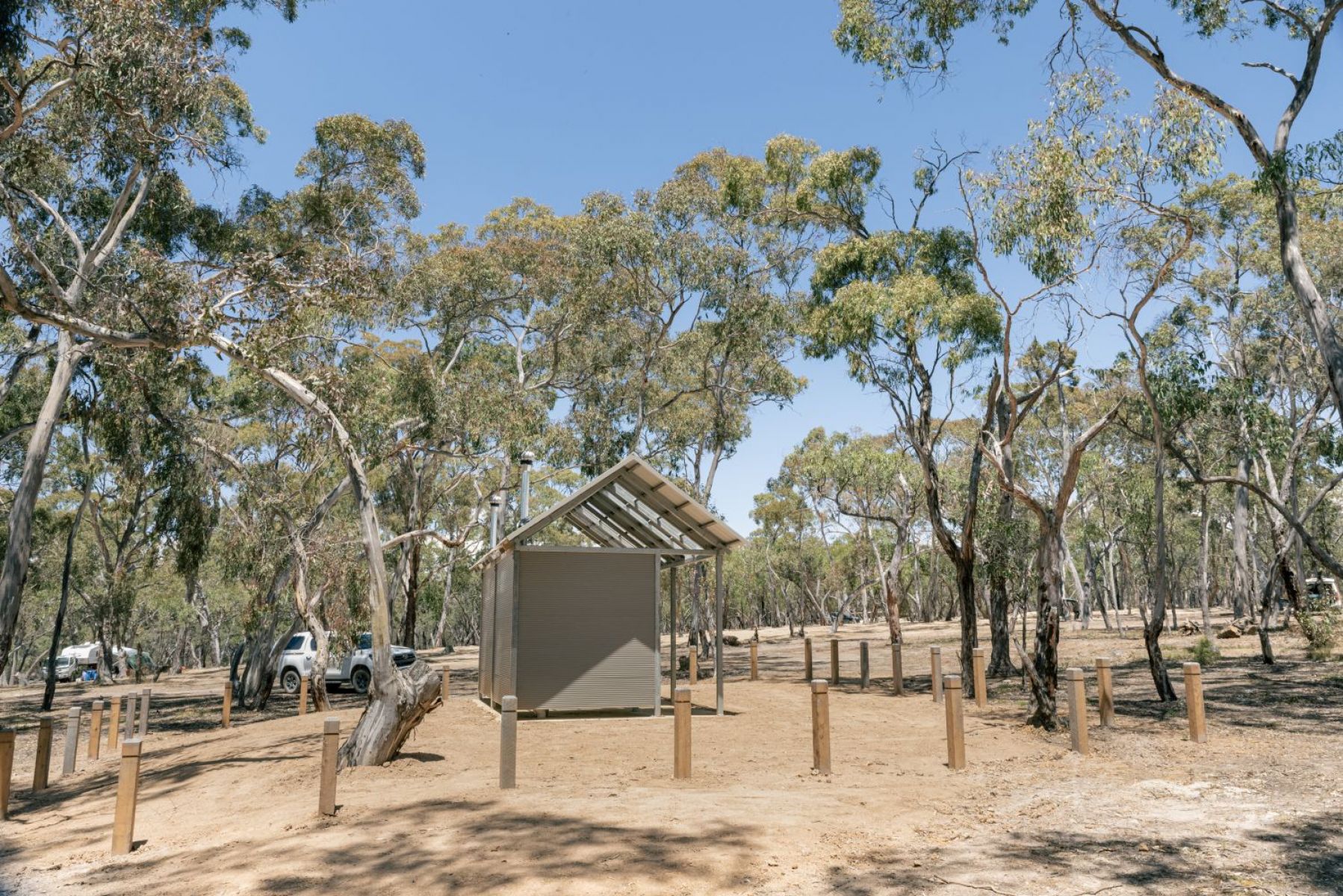 A small toilet block in bushland with cars and caravans in the background