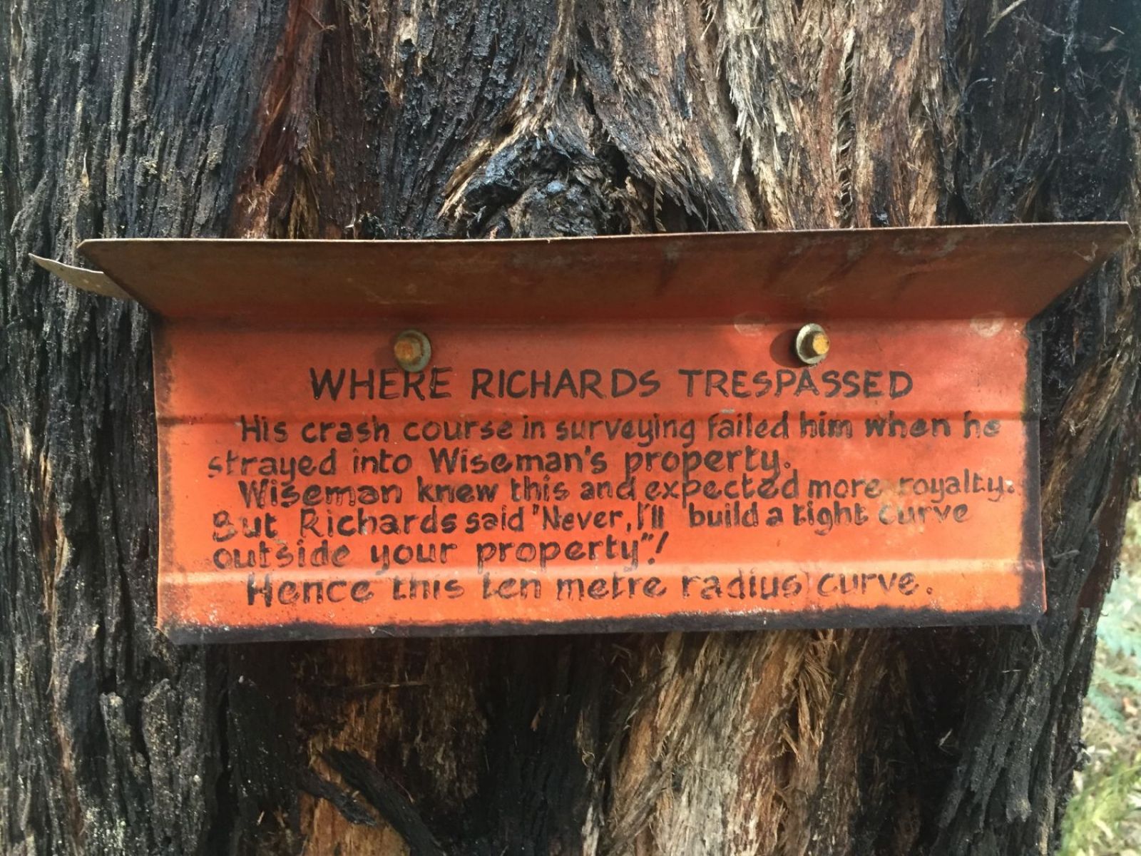 An orange sign pinned against a tree