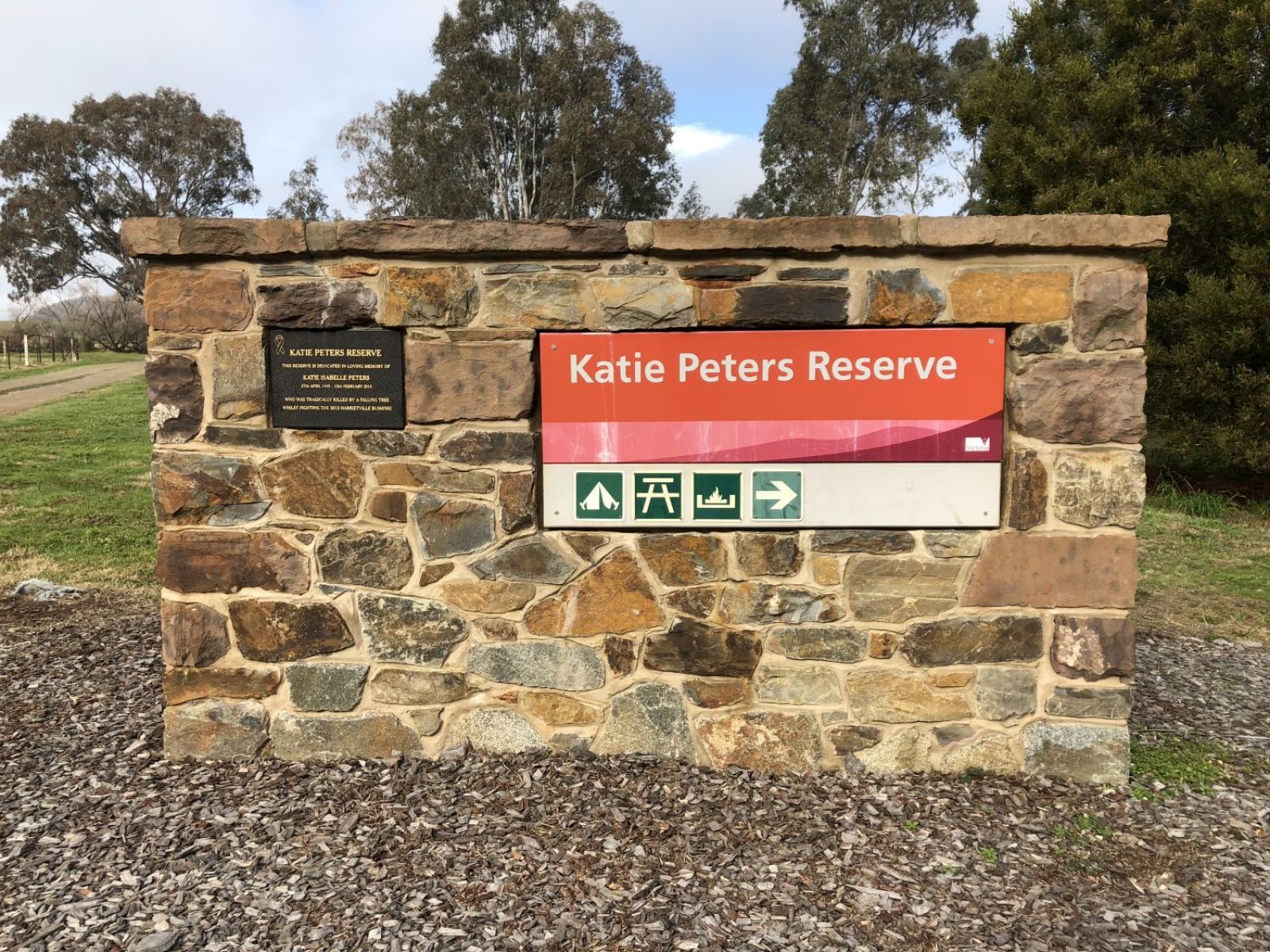 An orange informaiton sign reading Katie Peters Reserve on a stone crafted memorial wall.