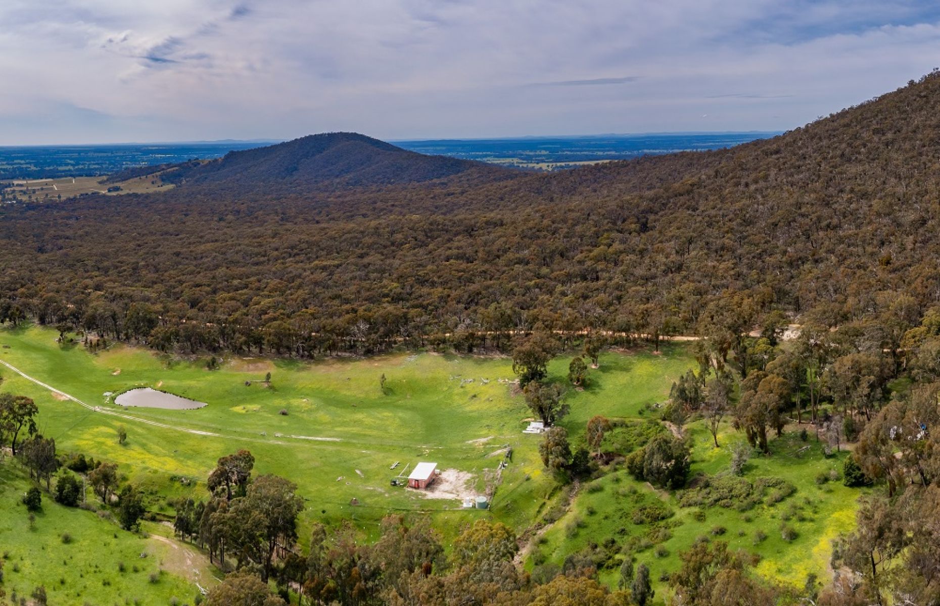 A birdseye view over a green grassy valley surrounded by hills with dense bushland 