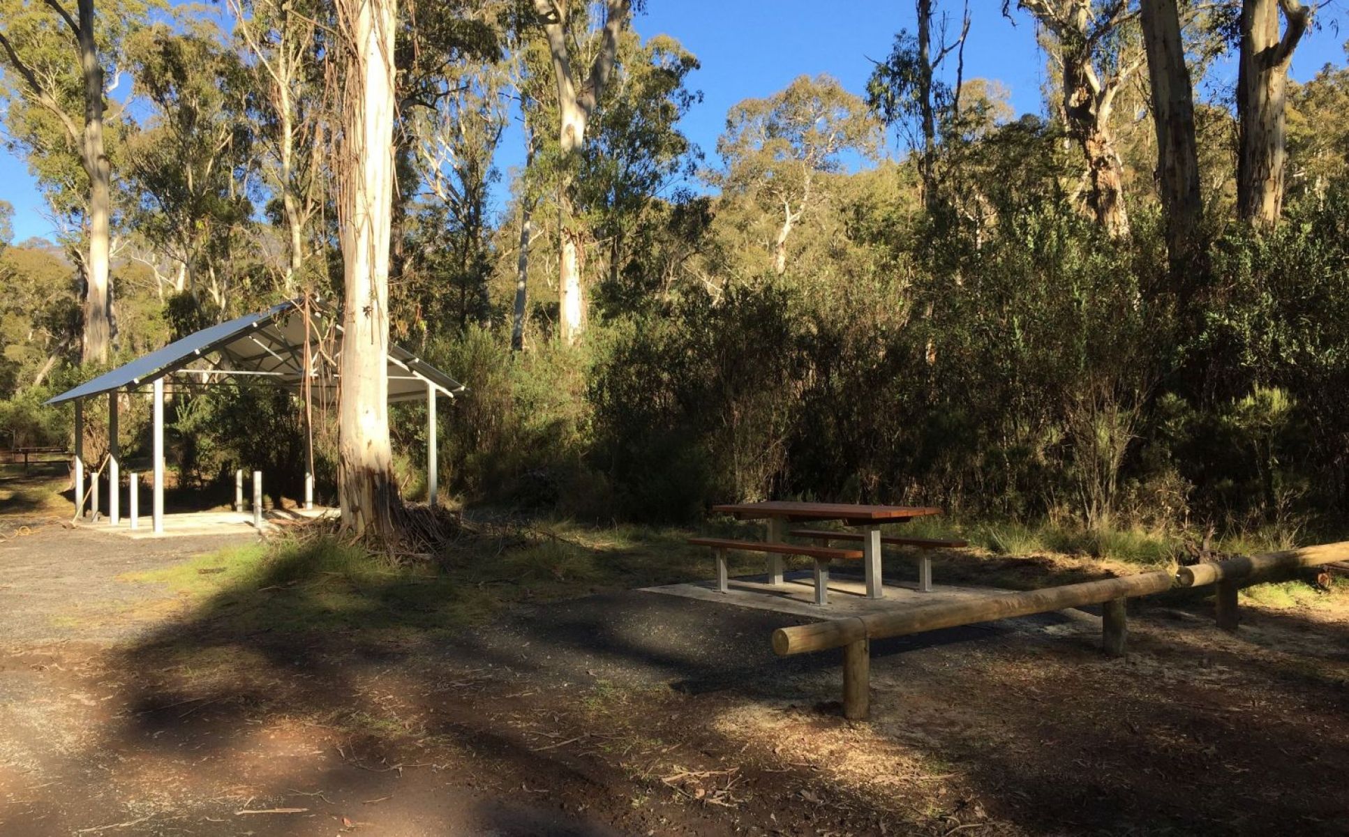 A picnic area with a metal shelter and table surrounded by bushland.